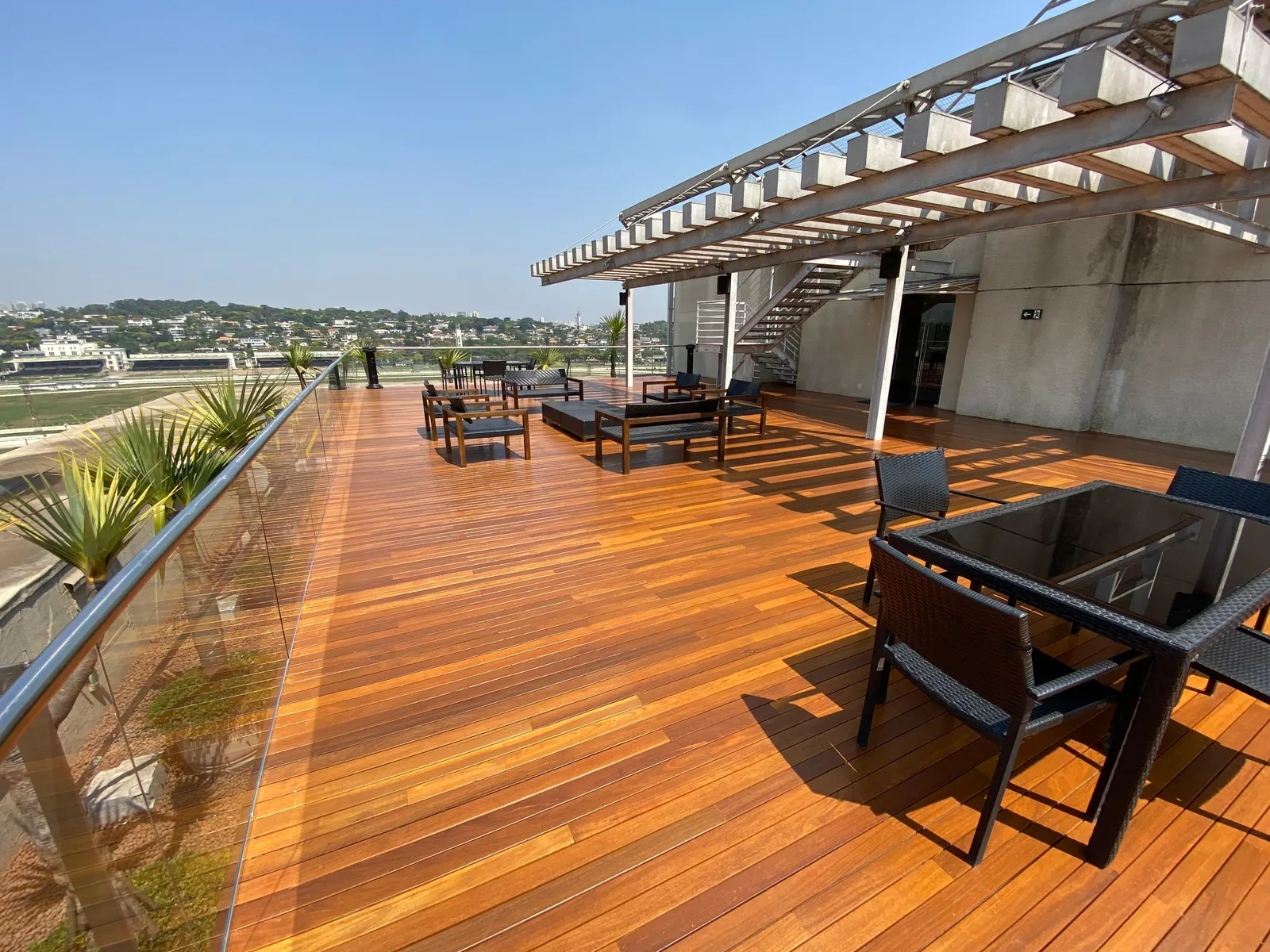 Terraço de cobertura com deck de madeira, pergolado e mobiliário de área externa no escritório Pinheiro Neto